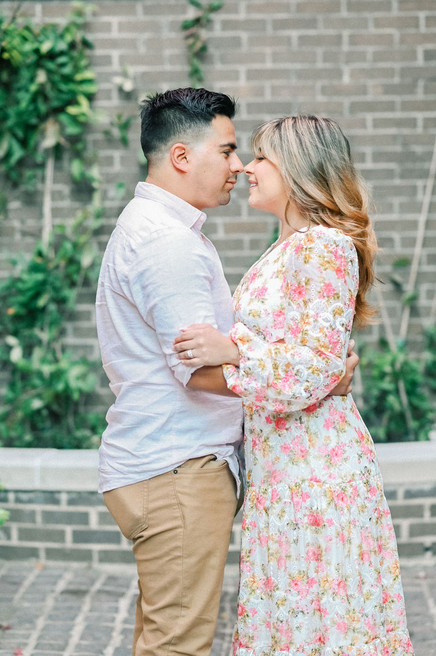 Couple nearly kissing while embracing outdoors in front of a lush green ivy-covered brick garden wall.