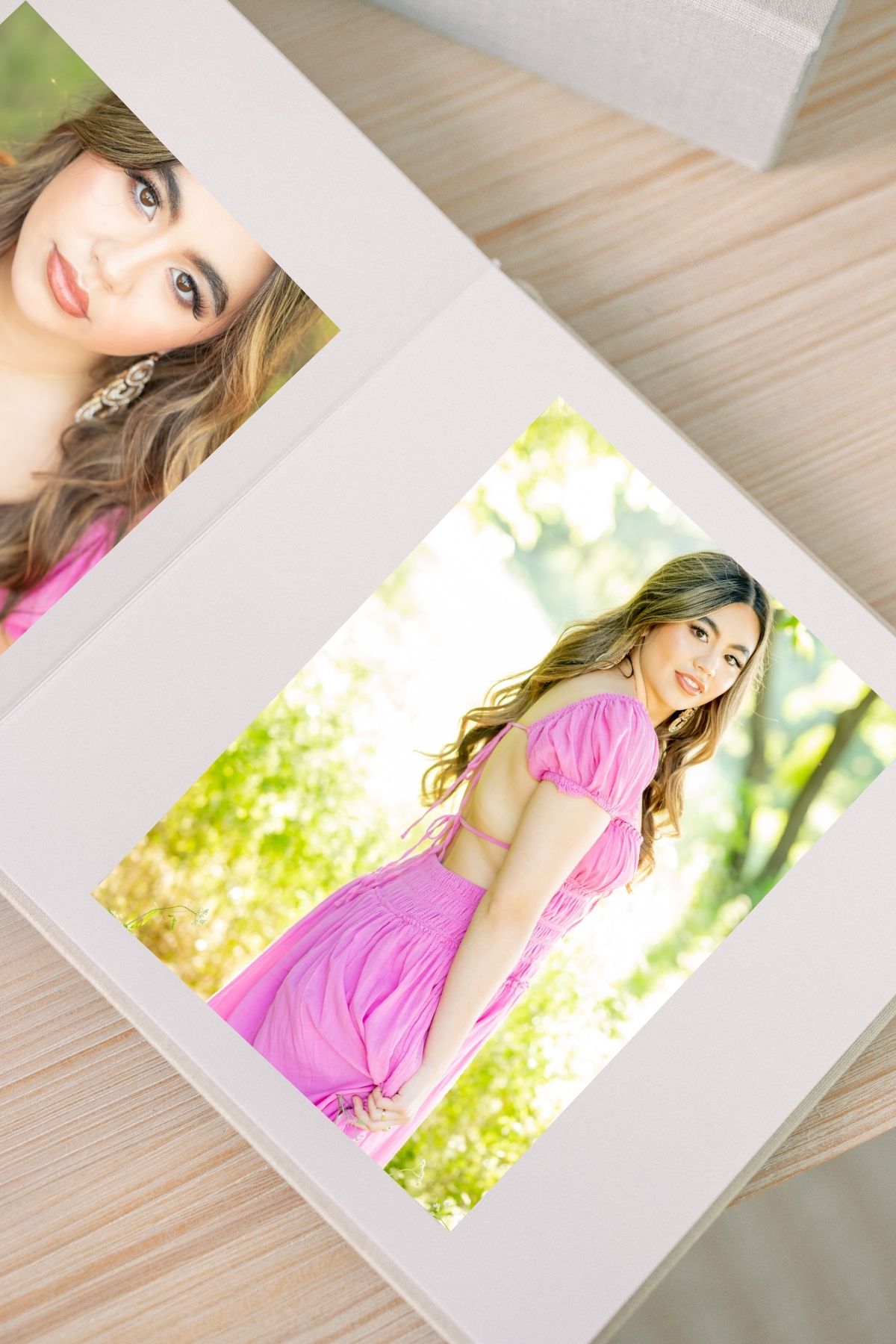 Two portrait photos of a young woman in a pink dress displayed in white photo mats on a wooden surface.
