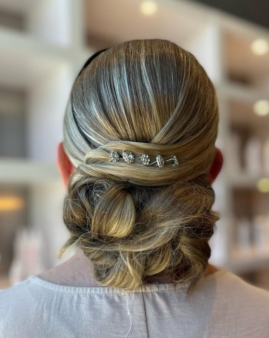 Elegant low updo hairstyle with rhinestone hair pins, featuring soft waves and highlights on brown hair.