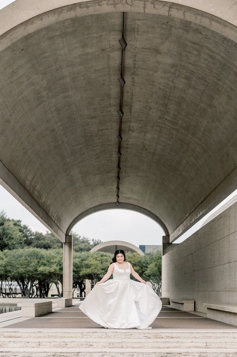 Bride twirling white wedding dress under dramatic curved concrete archway during bridal photo session.