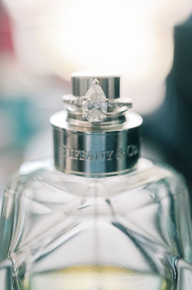 Tiffany & Co. perfume bottle topped with a pear-shaped diamond engagement ring and wedding band.