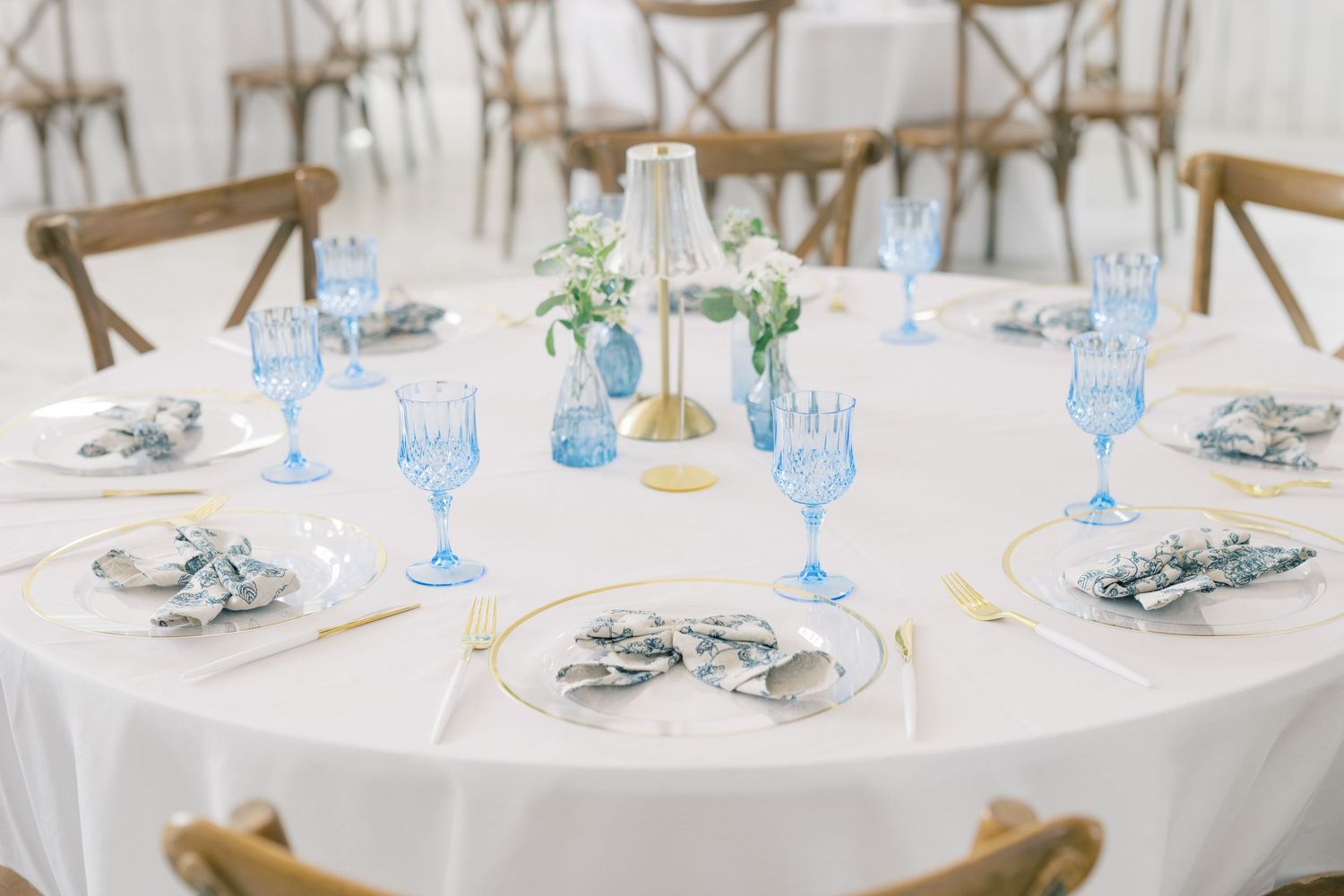 Elegant wedding reception table with blue goblets, gold accents, and white linens.
