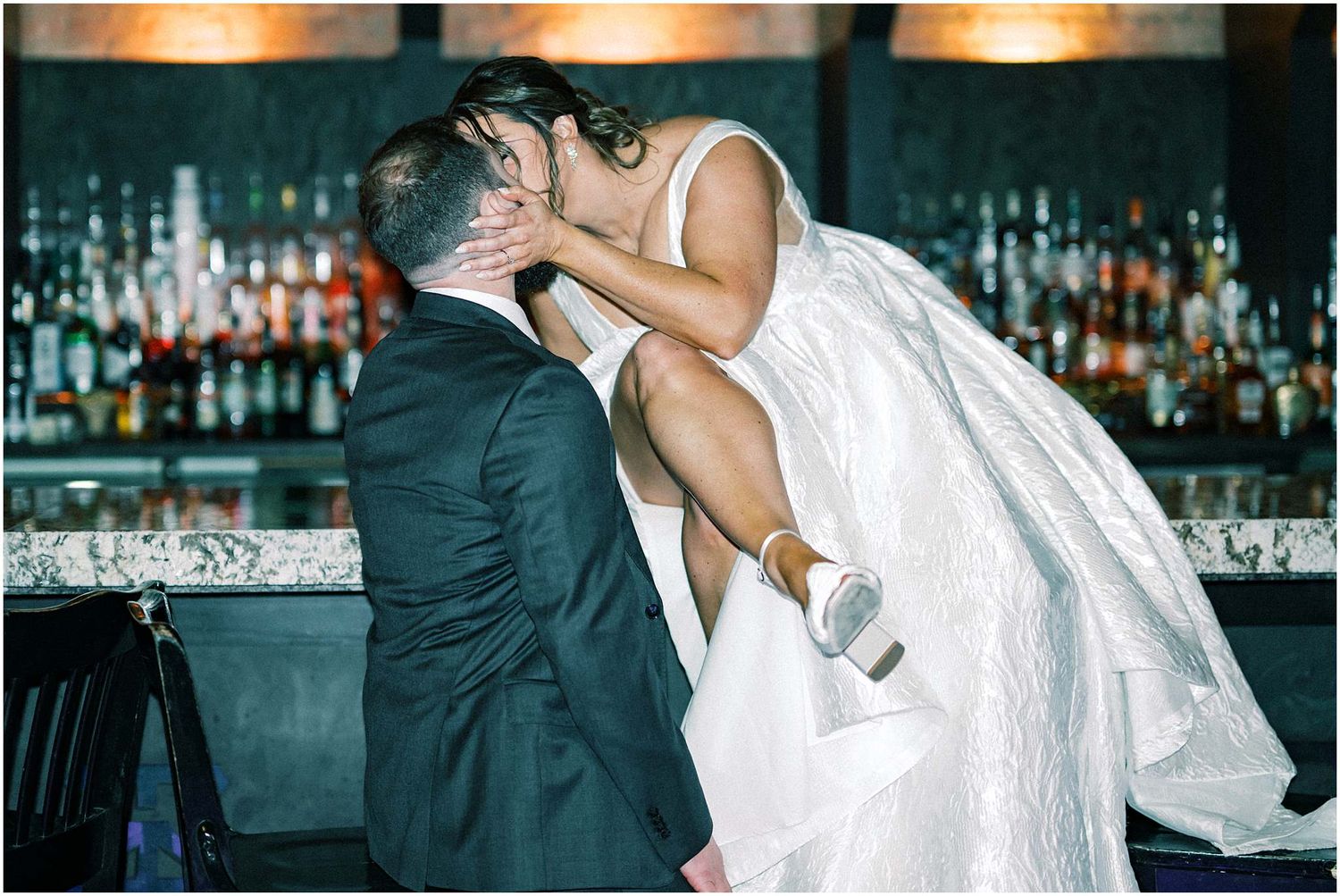 Couple sharing a romantic dance at their wedding reception in a dimly lit bar setting with warm lighting.