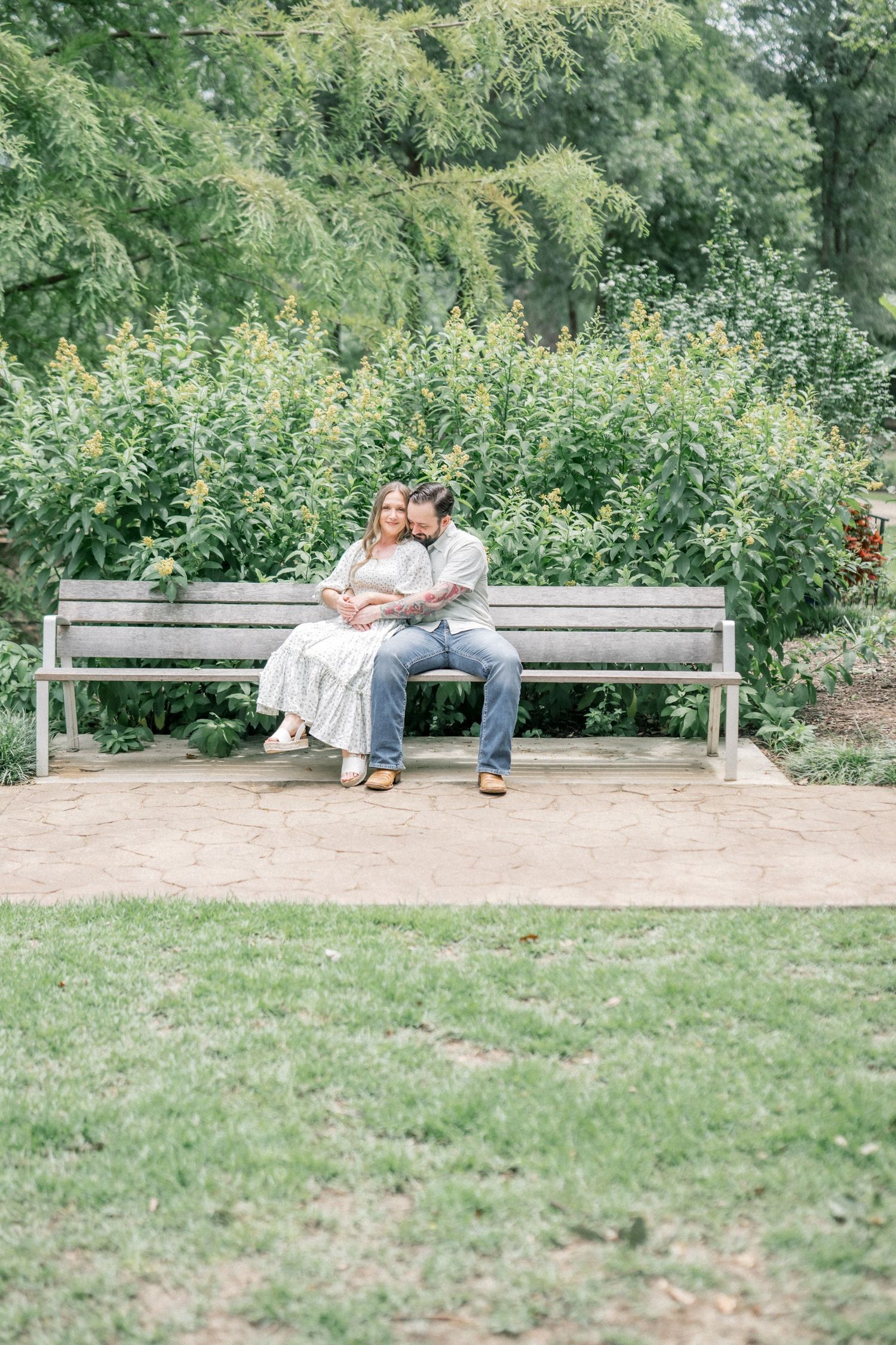 Couple sitting closely on a park bench surrounded by green foliage in a serene garden.