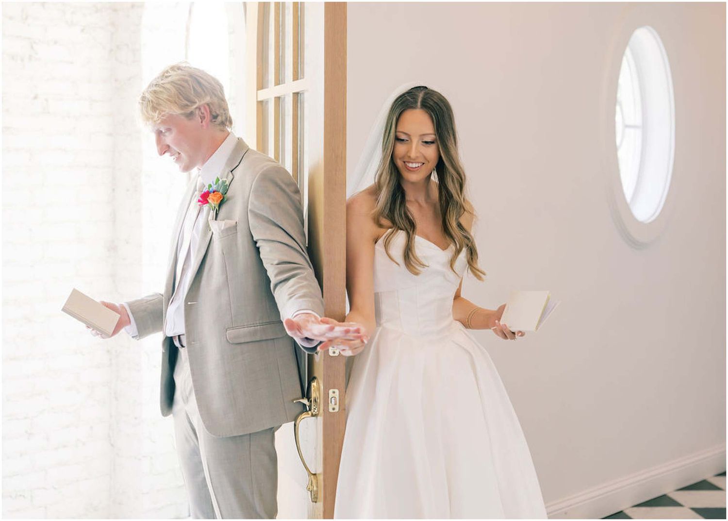 Bride in white gown smiles while exchanging vows with man in gray suit during intimate wedding ceremony indoors.