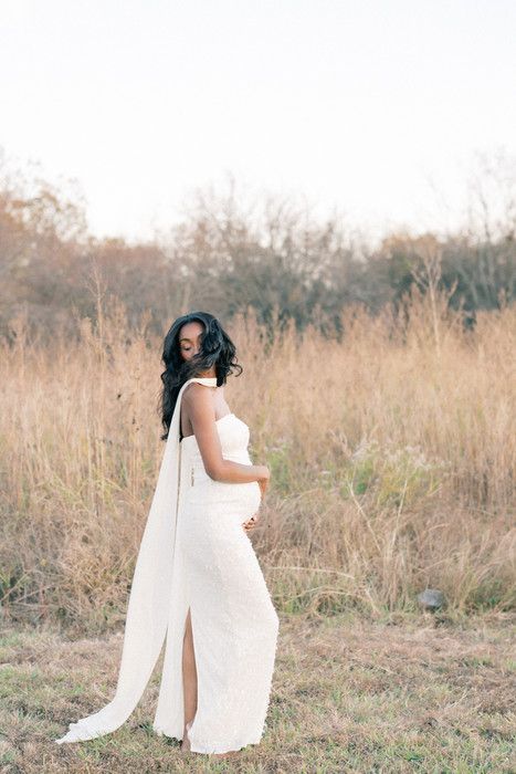 A dreamy maternity photoshoot captures a figure in white against tall grass and autumn trees.