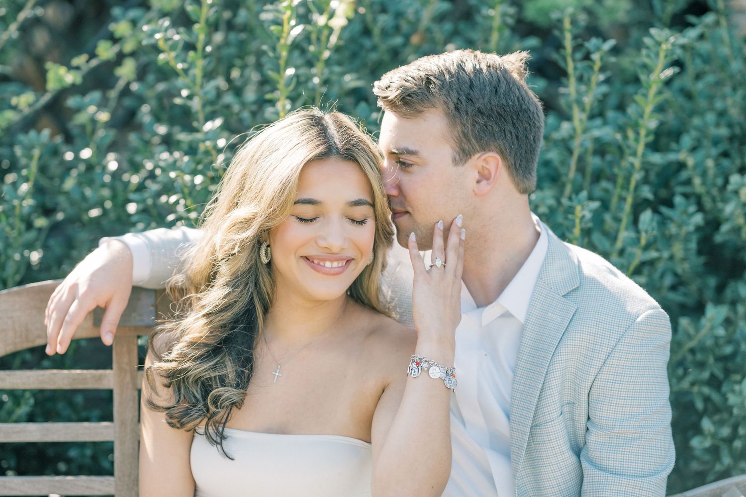 A romantic couple shares tender moments in a garden setting during an engagement or wedding photo session.