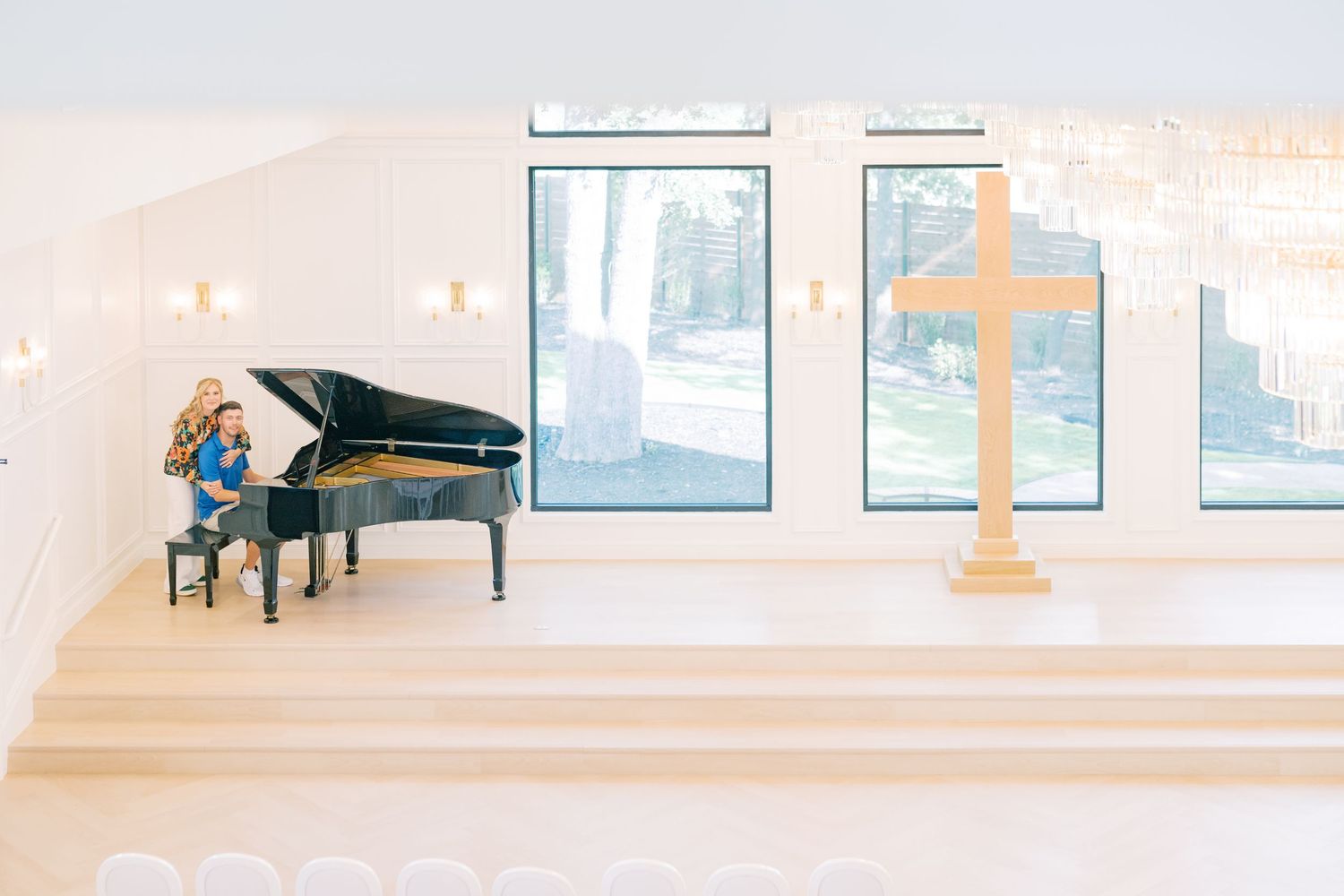 Couple sitting at a grand piano in a bright modern chapel with a wooden cross and large windows.