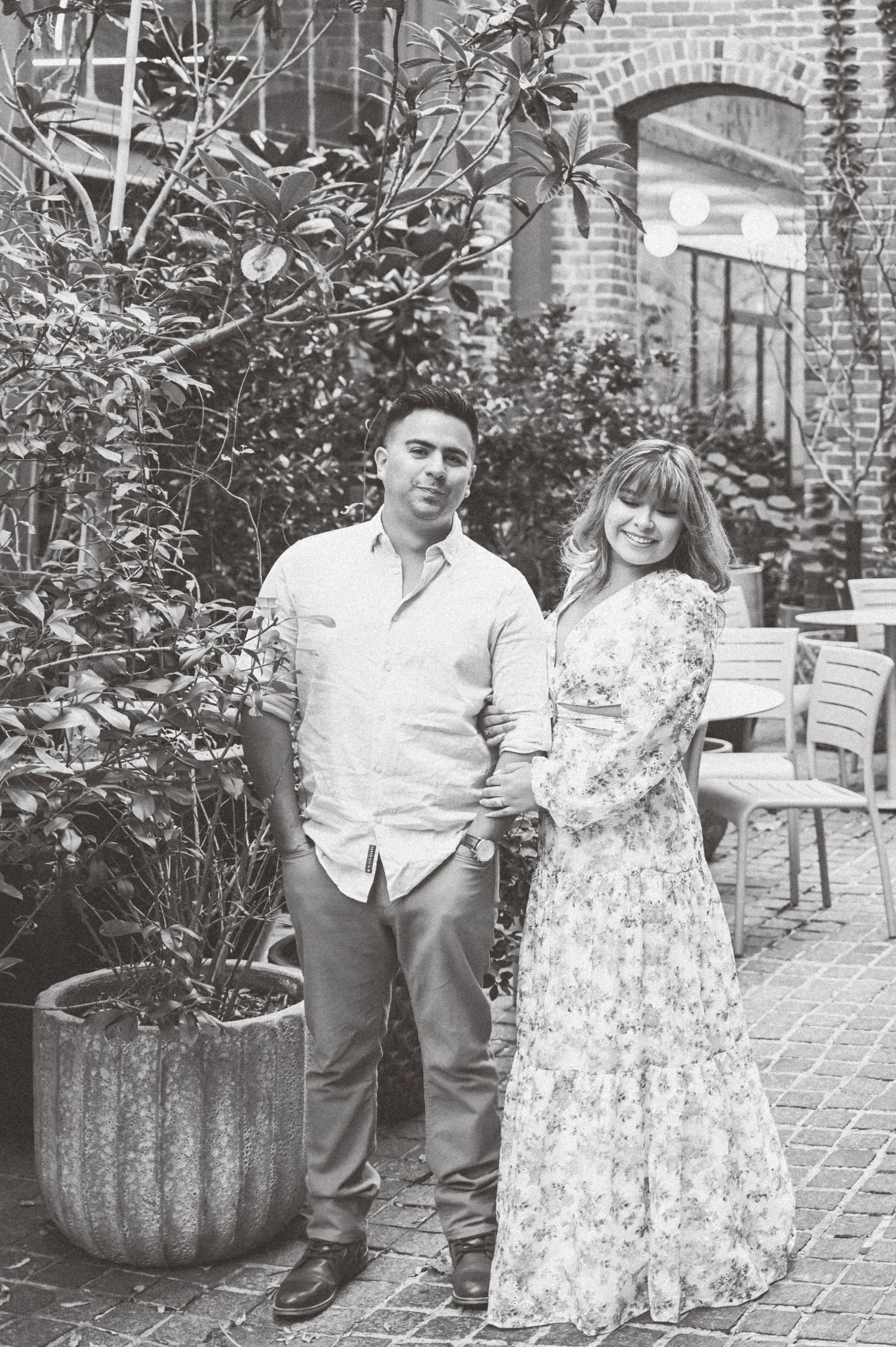 Black and white portrait of a couple standing together among greenery in a charming courtyard.