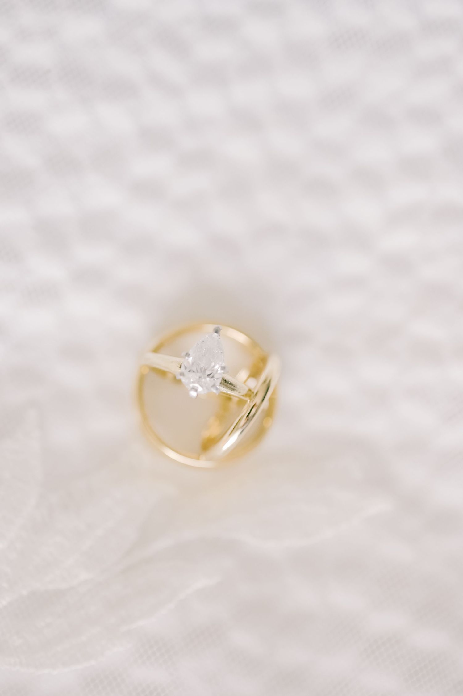 Gold engagement ring with pear-shaped diamond solitaire paired with a wedding band on white textured fabric.