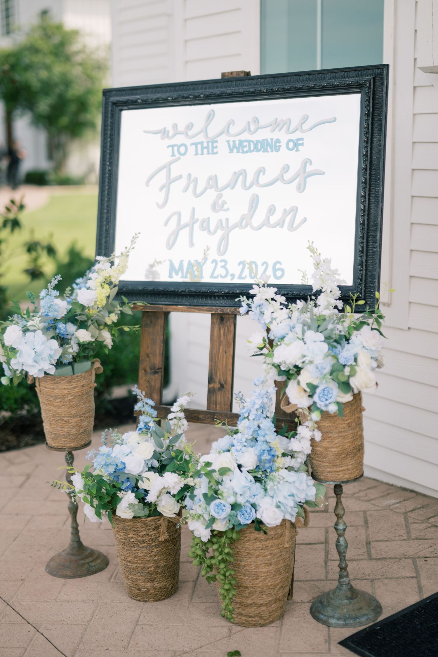 Wedding welcome sign for Frances and Hayden May 23 2026 with blue floral arrangements.