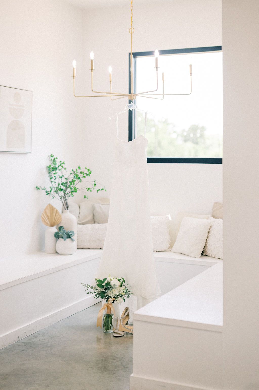 Bright white bathroom with gold chandelier, floral bouquet, and cozy window seat with neutral pillows.