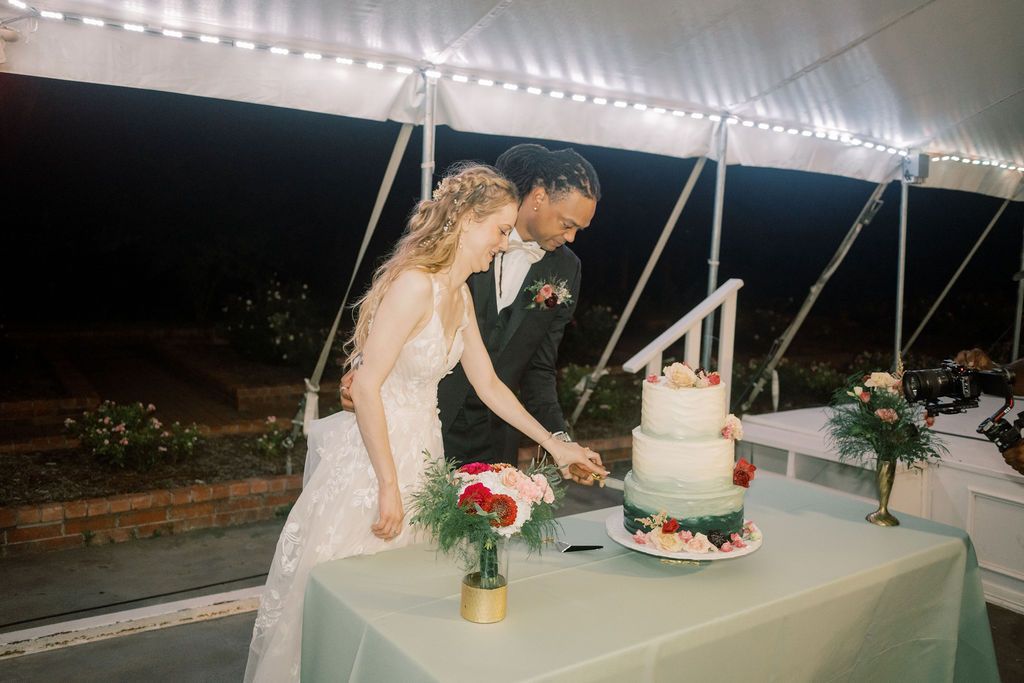 Bride and groom cutting their elegant three-tier wedding cake under a white tent at a night reception.