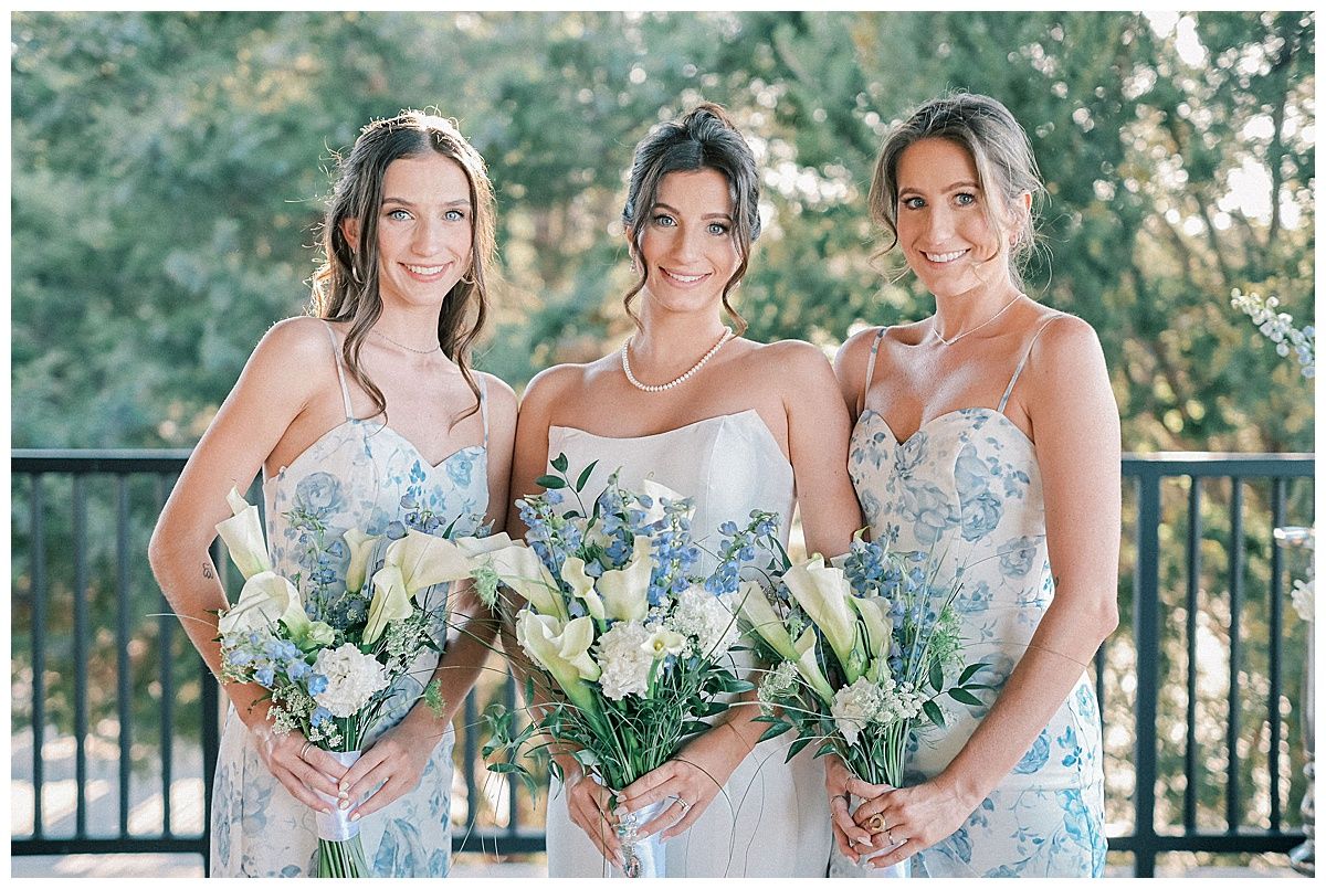 Bridesmaids in light blue floral dresses holding white and green bouquets.