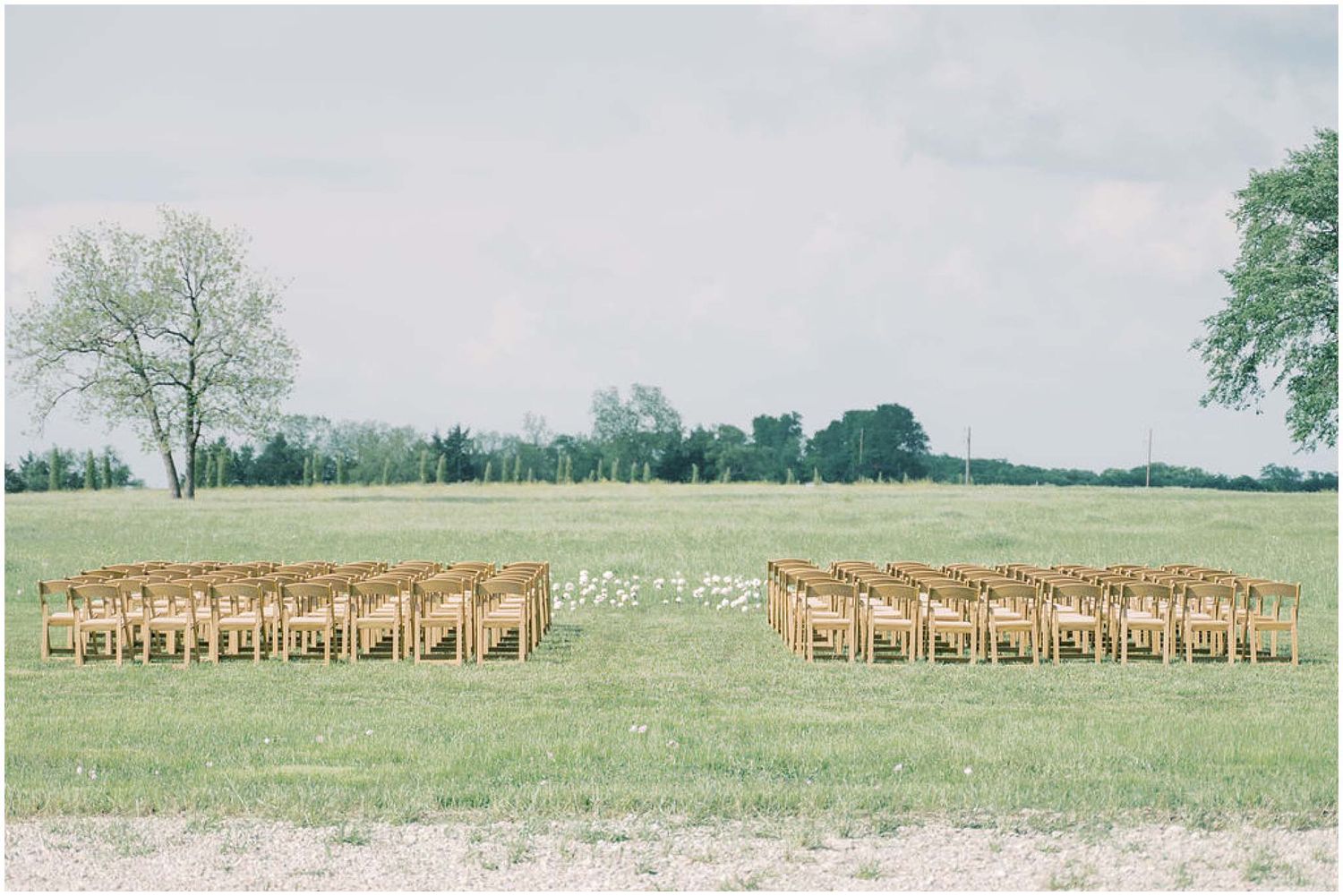Rows of wooden chairs set up outdoors for a wedding ceremony on a grassy field.