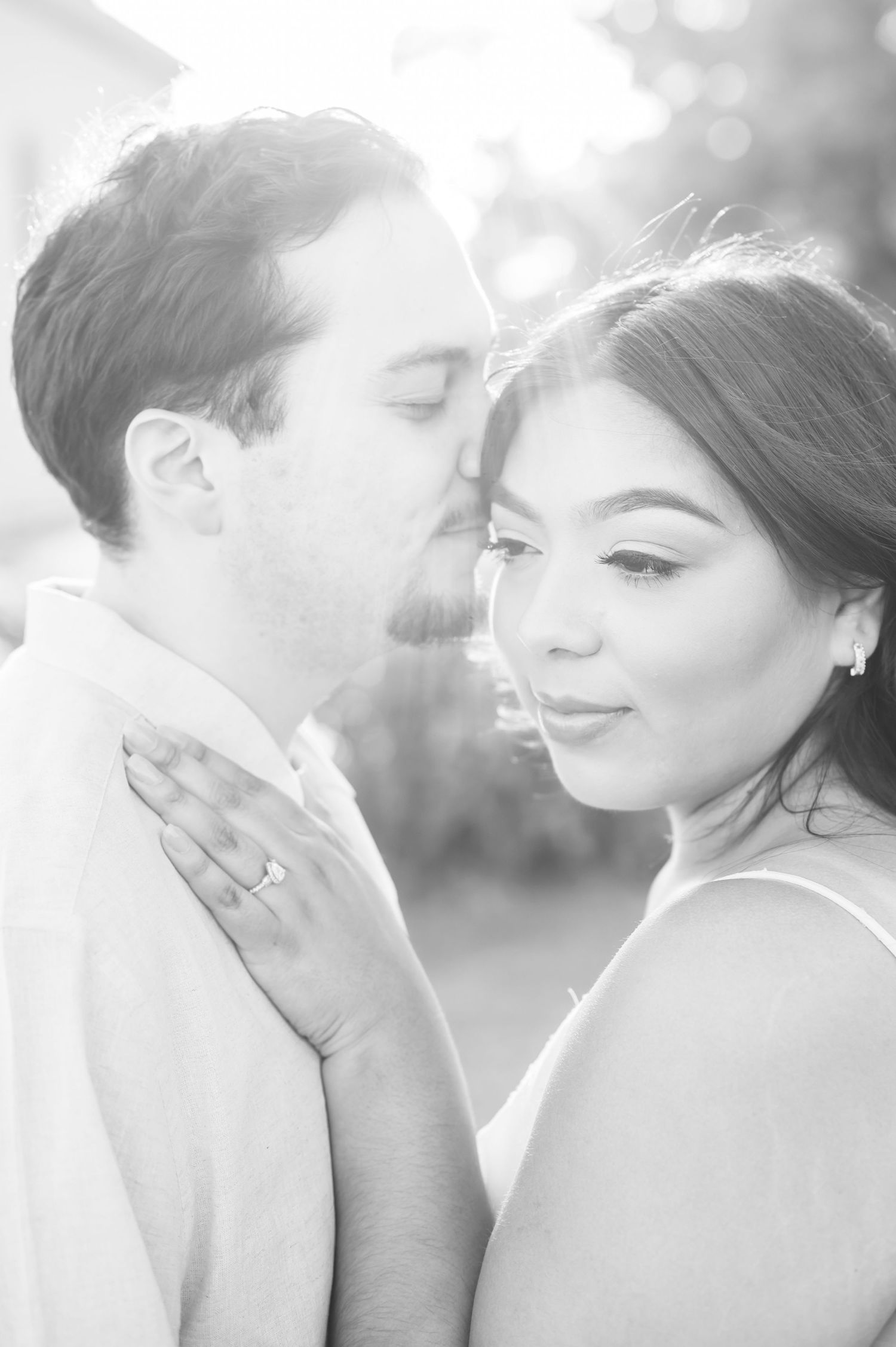 A black and white romantic portrait of a couple in an intimate embrace with soft backlighting.