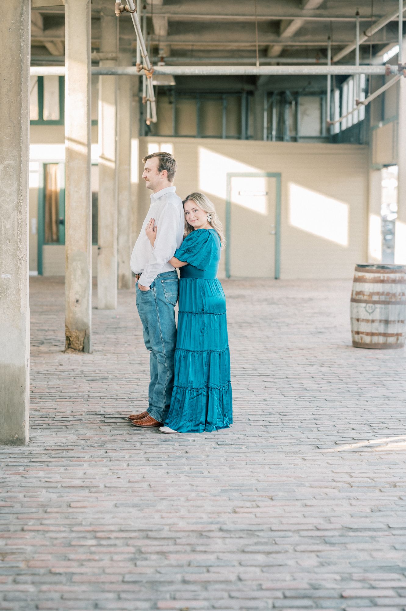 Couple shares intimate moments in a sunlit brick-floored industrial space.