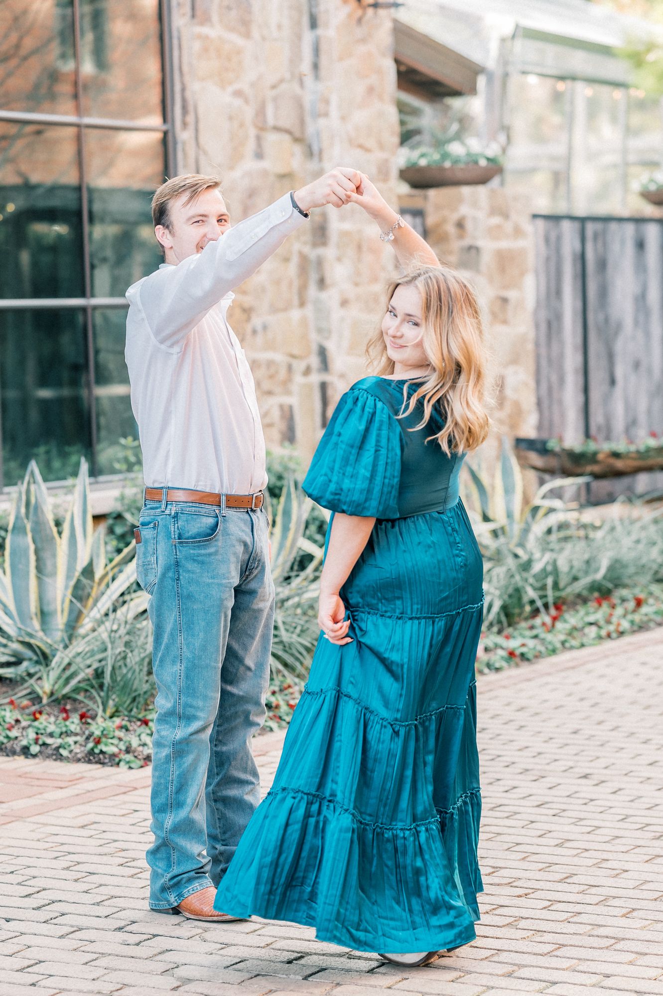 A dancing couple spins joyfully on a stone patio with the woman wearing a flowing teal dress.