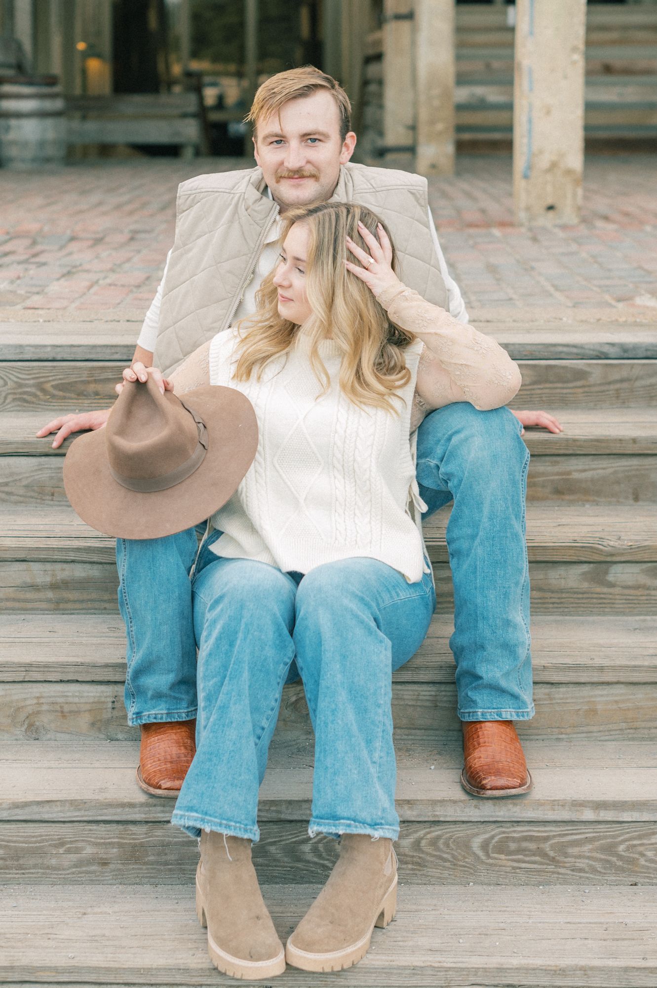 Couple sitting on wooden steps wearing jeans and casual attire in a rustic outdoor setting.