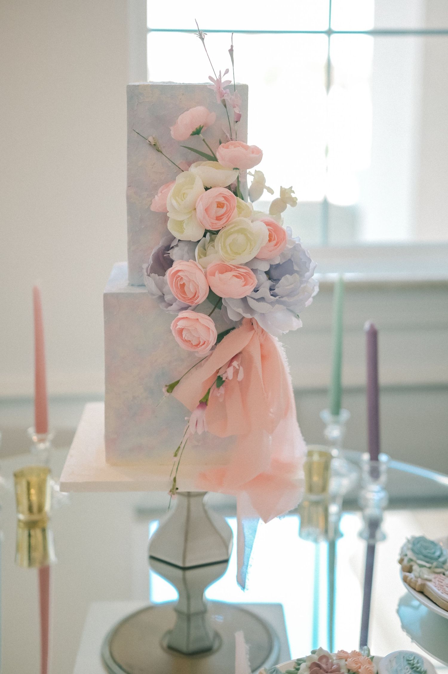 Elegant wedding cake decorated with soft pink and blue flowers and white candles.