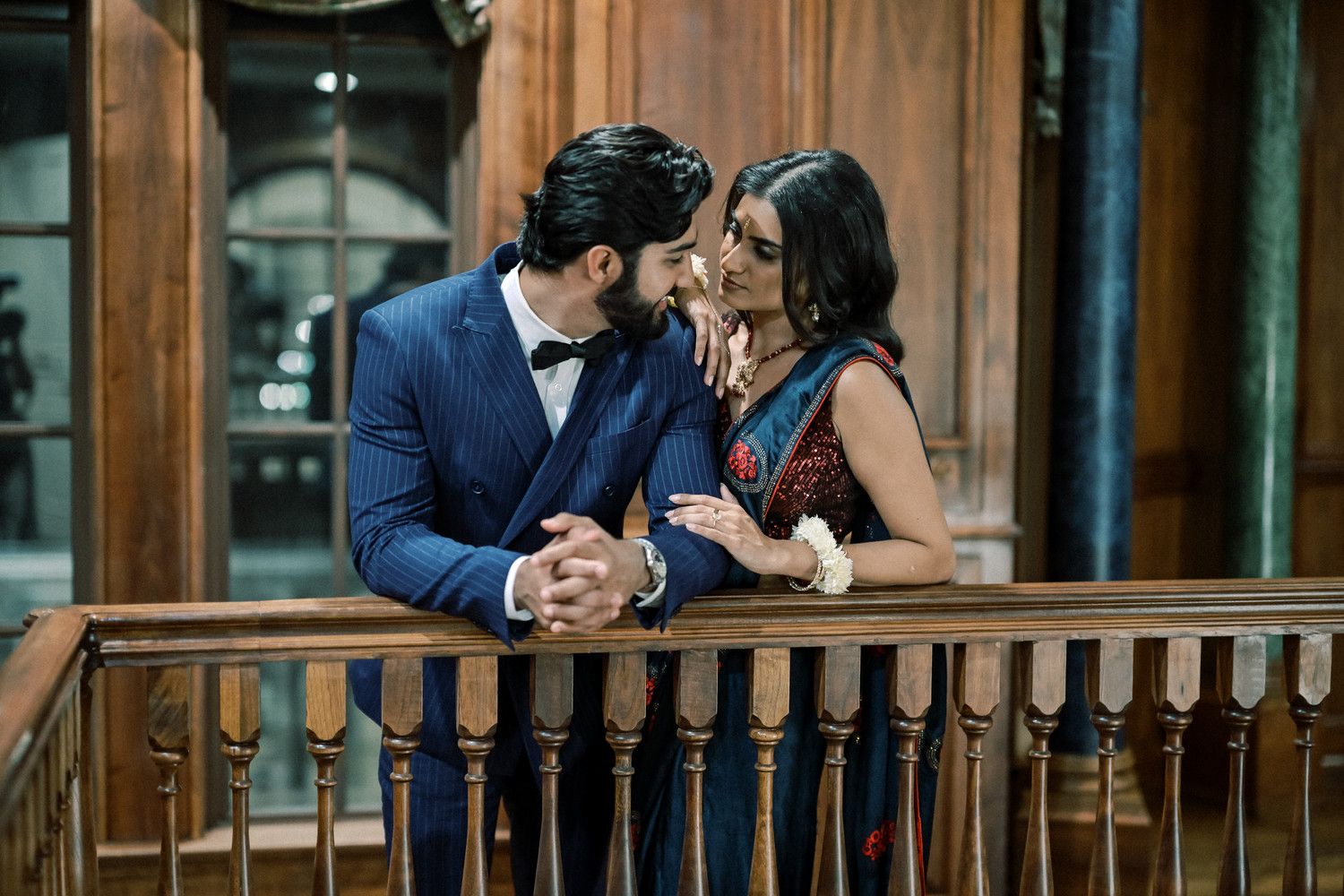 Romantic couple embraces in an elegant wood-paneled hallway beneath ornate chandeliers.
