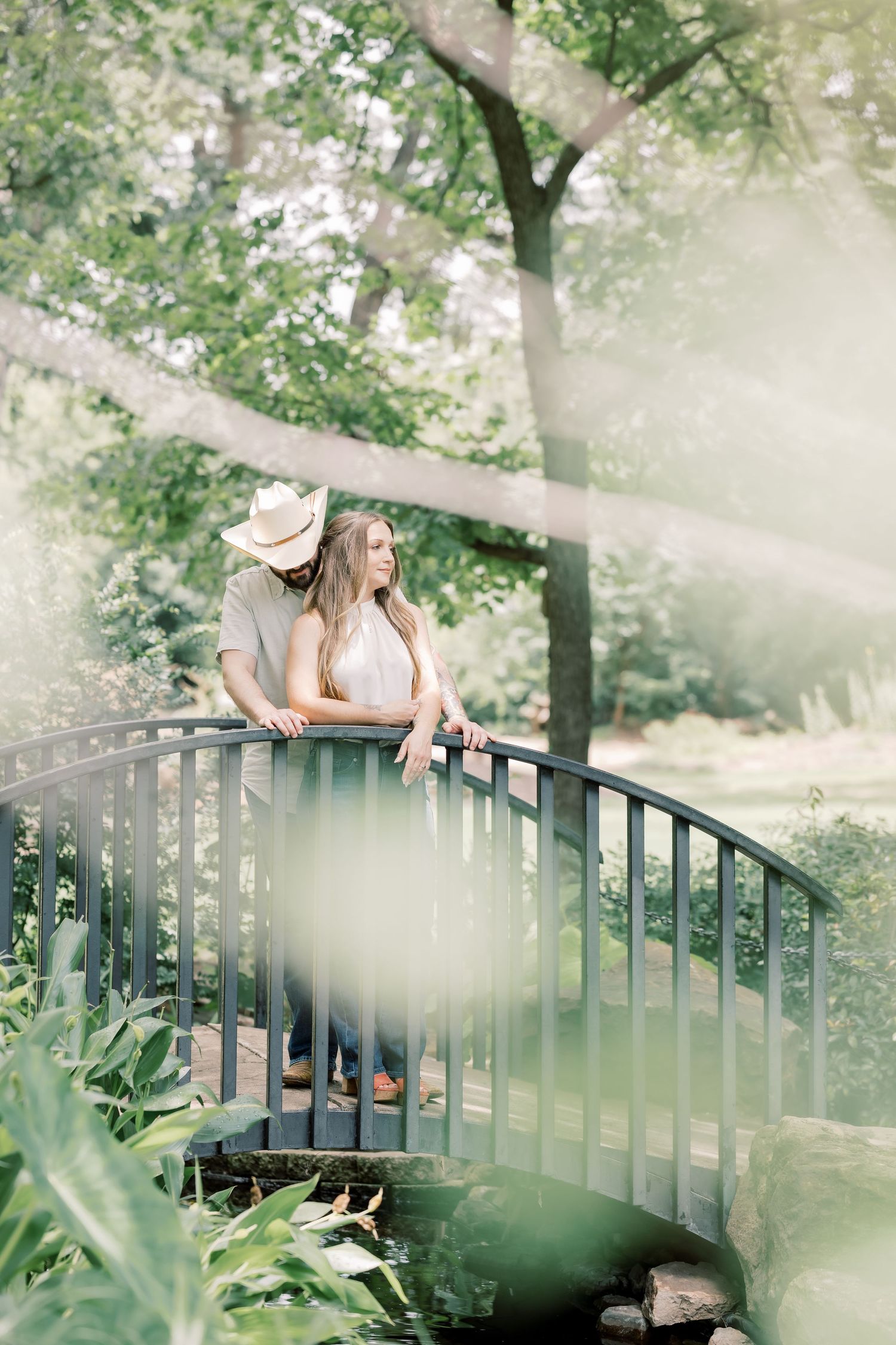 Couple sharing a romantic moment on a curved garden bridge surrounded by lush green trees.