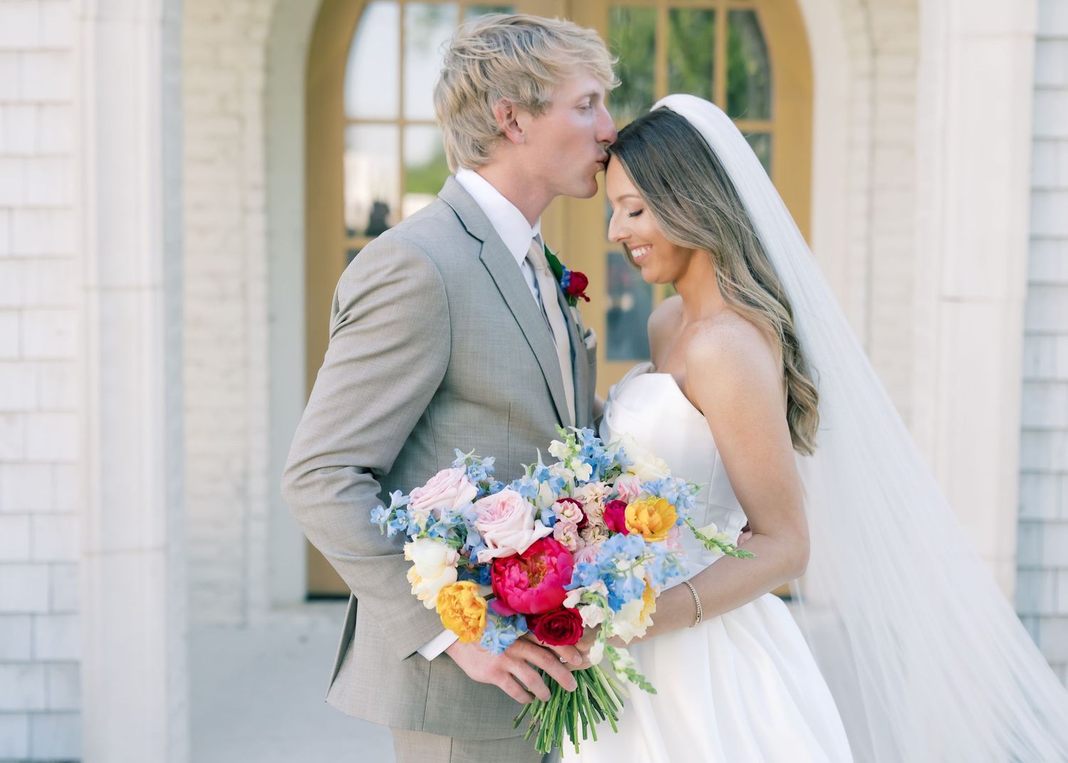 Bride and groom sharing a kiss outdoors, bride holding vibrant mixed floral bouquet.