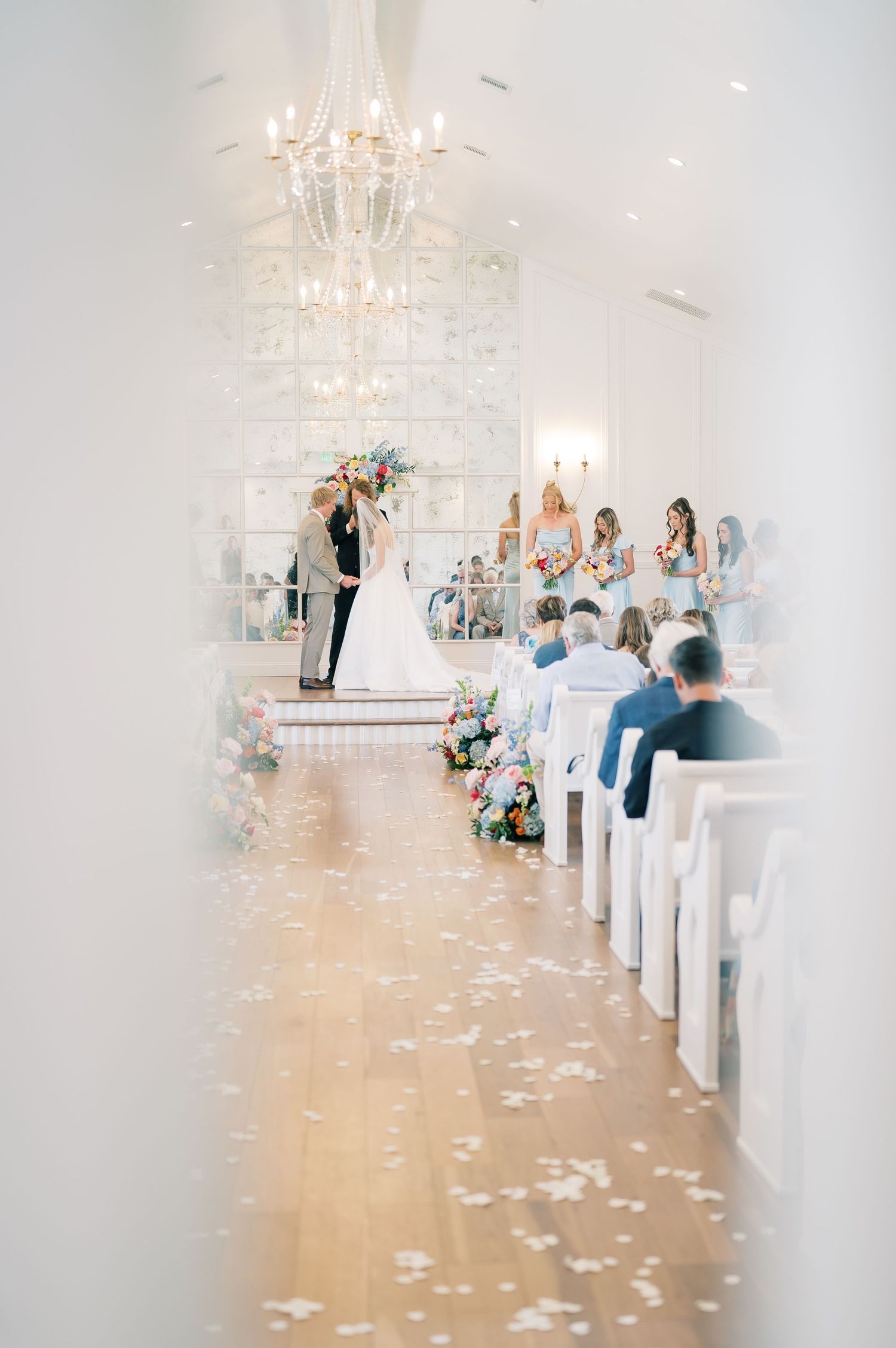 Elegant white chapel wedding ceremony with floral aisle decor and chandelier.