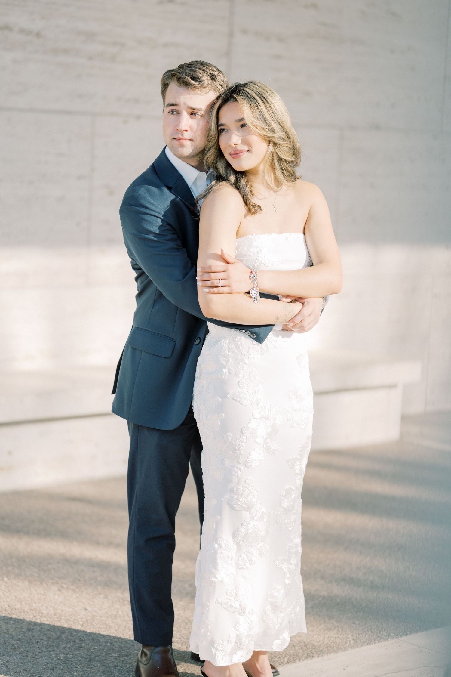 A couple embraces in a romantic moment, with the bride wearing a white lace dress and groom in a navy suit.