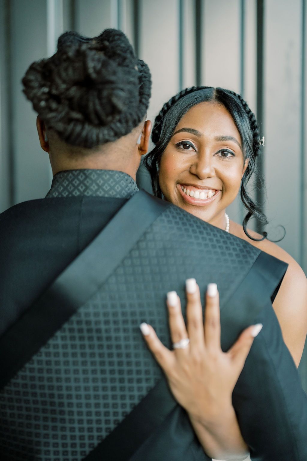 Smiling bride in black dress hugs groom, showcasing her engagement ring, in an elegant wedding portrait.