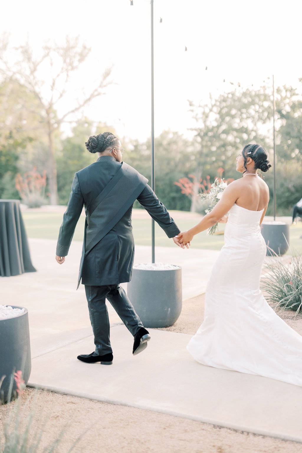 Bride and groom walking hand in hand outdoors at their wedding venue during golden hour.