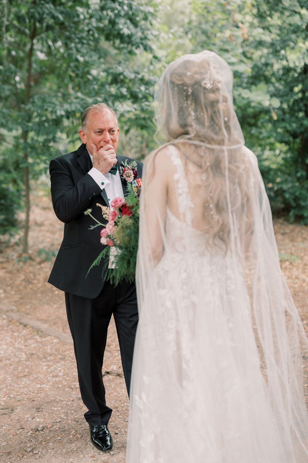 Emotional father tears up seeing bride daughter in wedding gown and veil during first look outdoor ceremony.