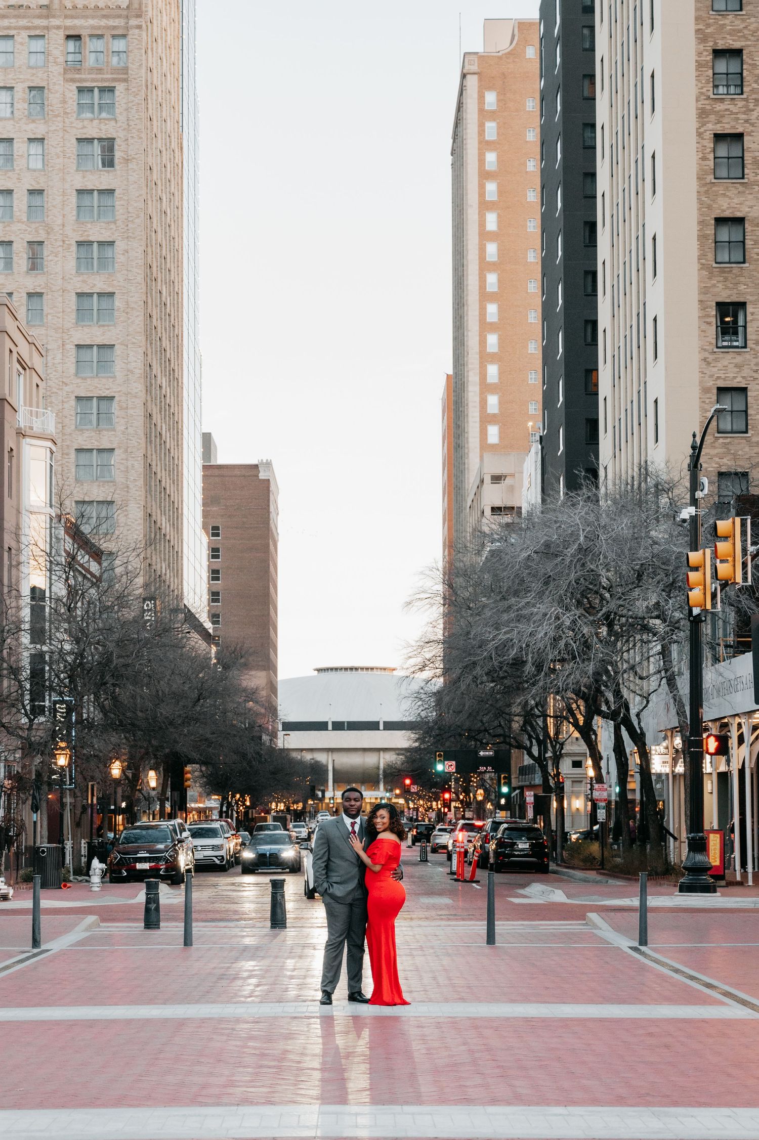 Couple posing on urban city street, woman in red maternity gown, tall buildings.