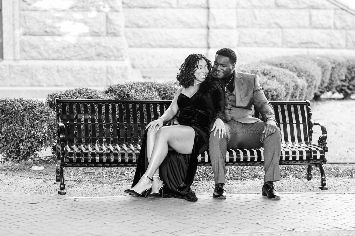 Stylish black and white portrait of a couple laughing together on an outdoor bench.