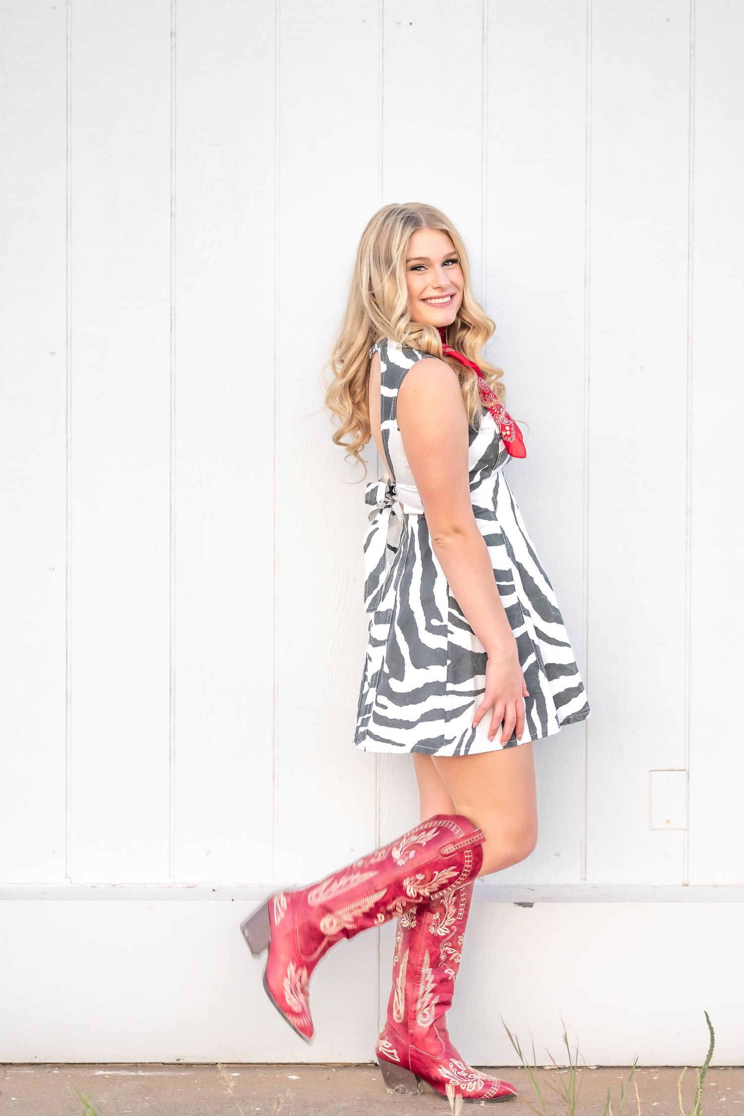 Blonde woman in zebra print mini dress and red cowboy boots posing against white wall.