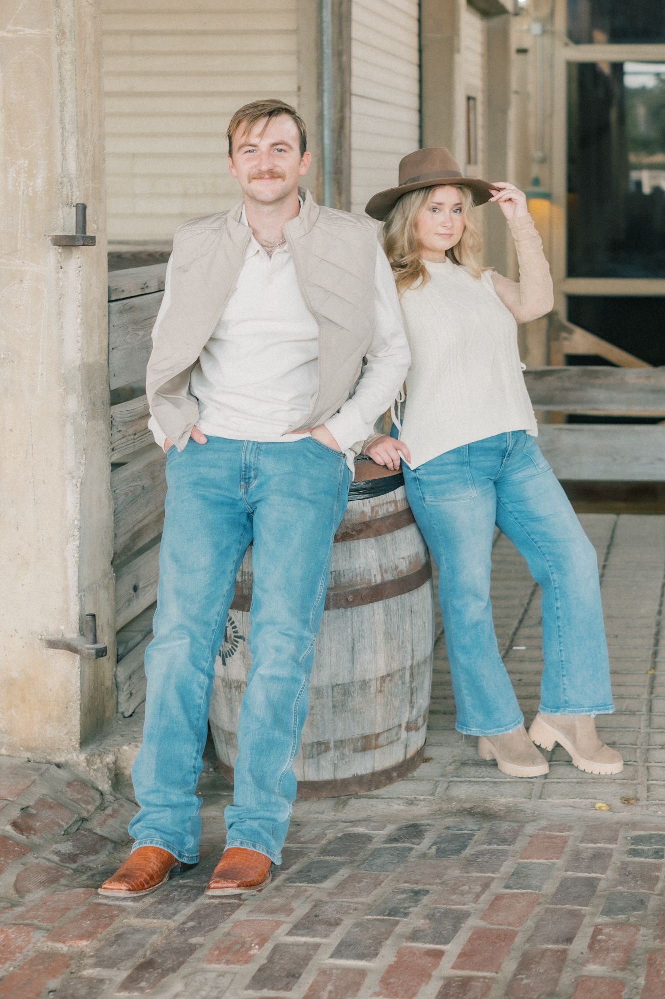 A couple sits together on rustic wooden barrels against a white building exterior.