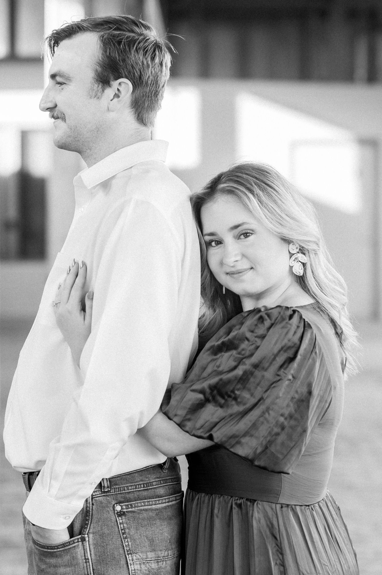 A romantic black and white engagement photo of a couple posing back to front in casual attire.