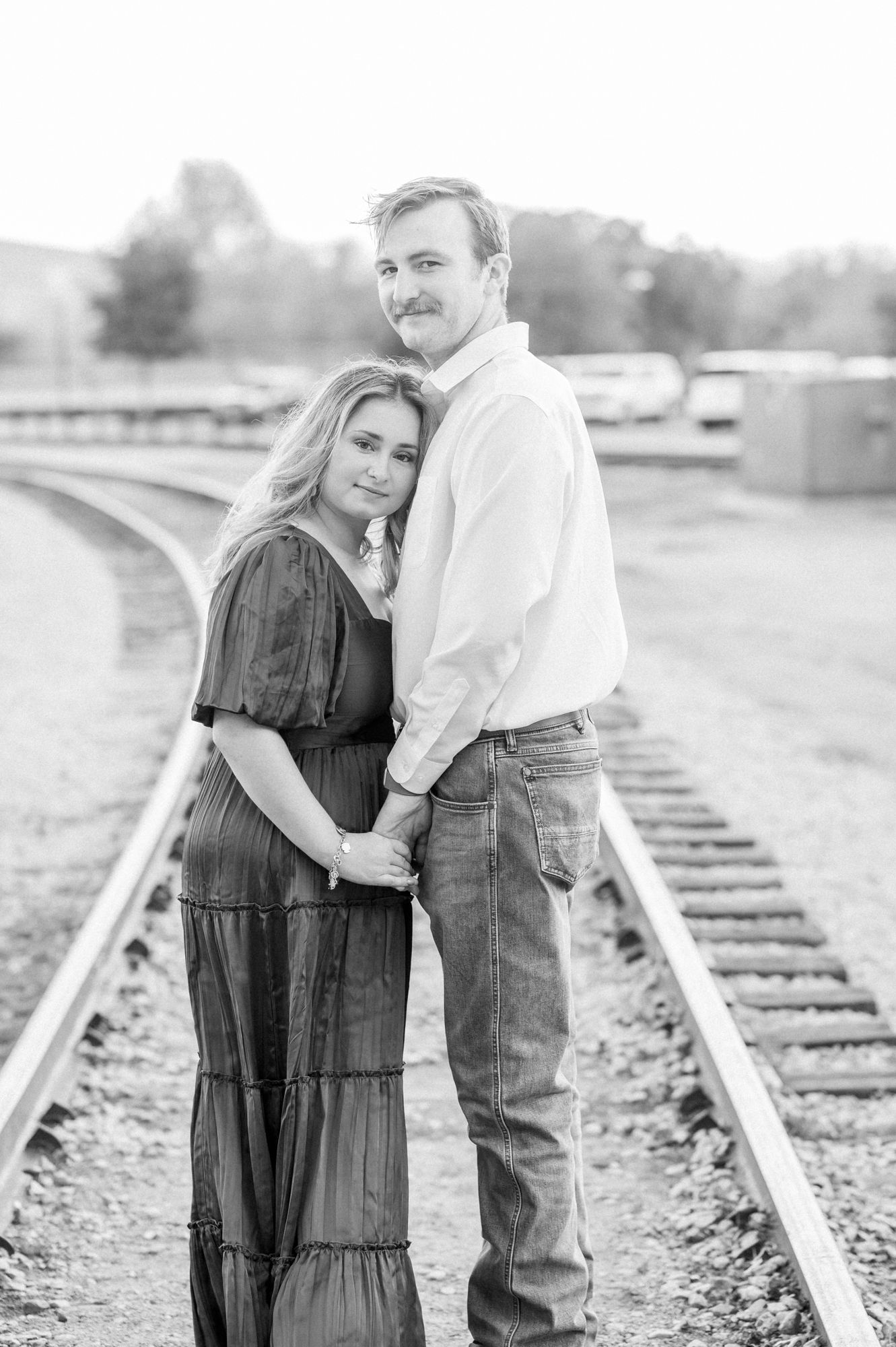Black and white engagement portraits captured along rustic railroad tracks in a rural setting.