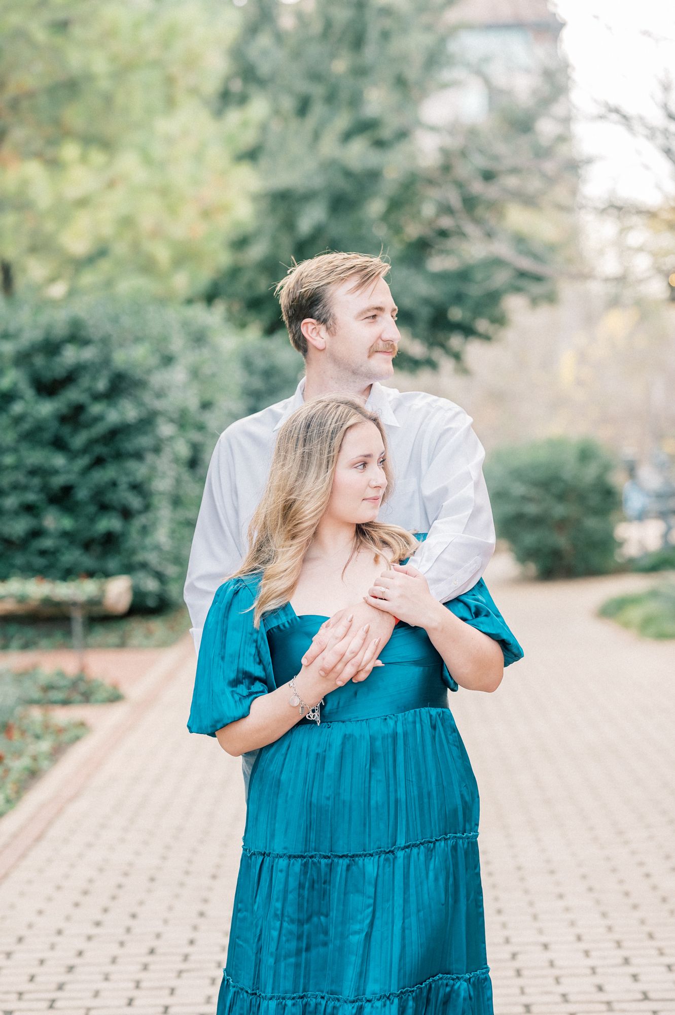 A couple shares a tender moment outdoors, with one wearing a vibrant teal dress during their photo session.