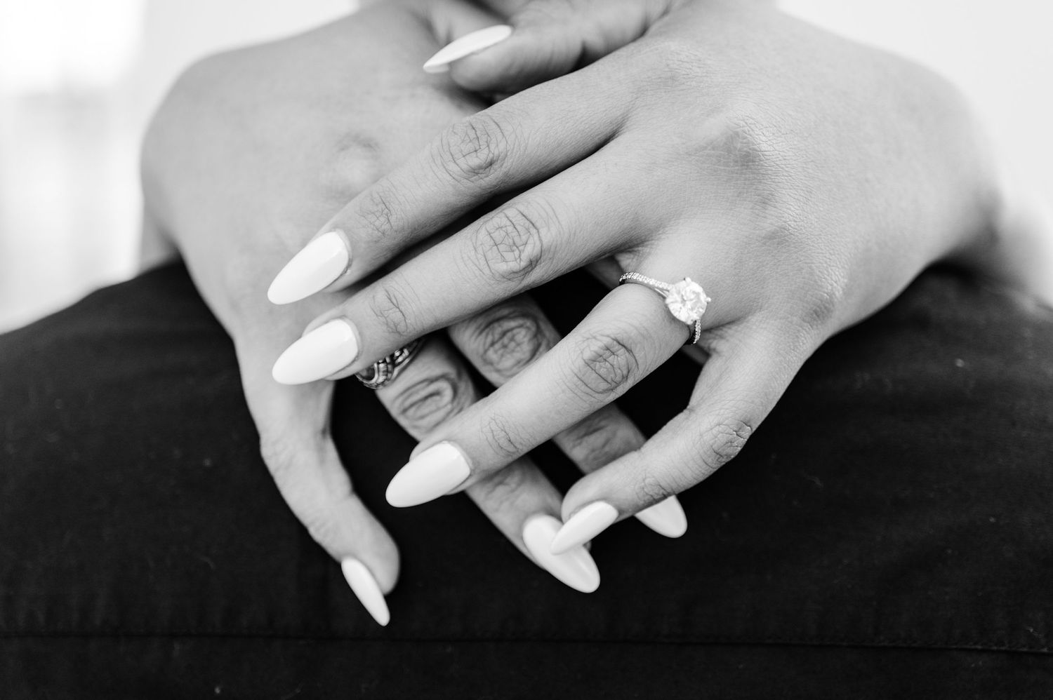 Black and white close-up of hands with white manicured nails and an engagement ring.