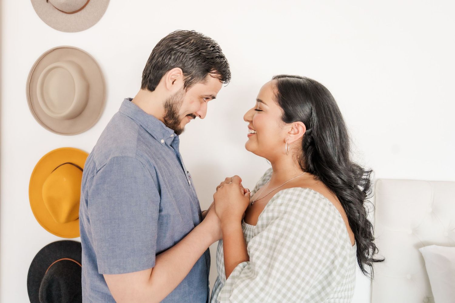 A tender moment between a couple during a maternity session with decorative hats on the wall.