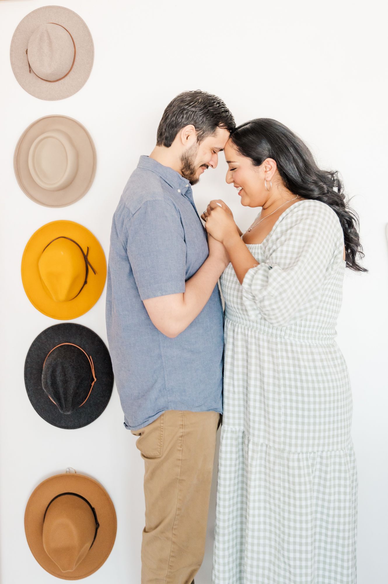 A couple poses playfully against a white wall decorated with brown and yellow decorative plates.