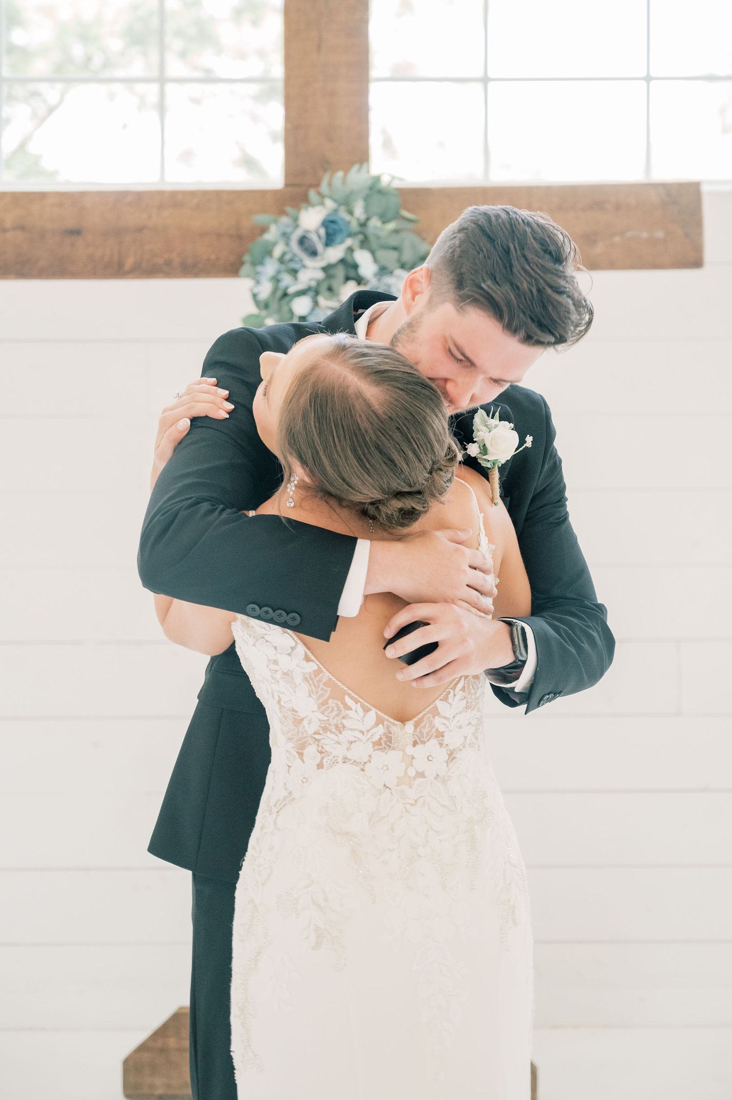 Emotional first look between newlyweds in a bright white indoor venue with natural lighting.