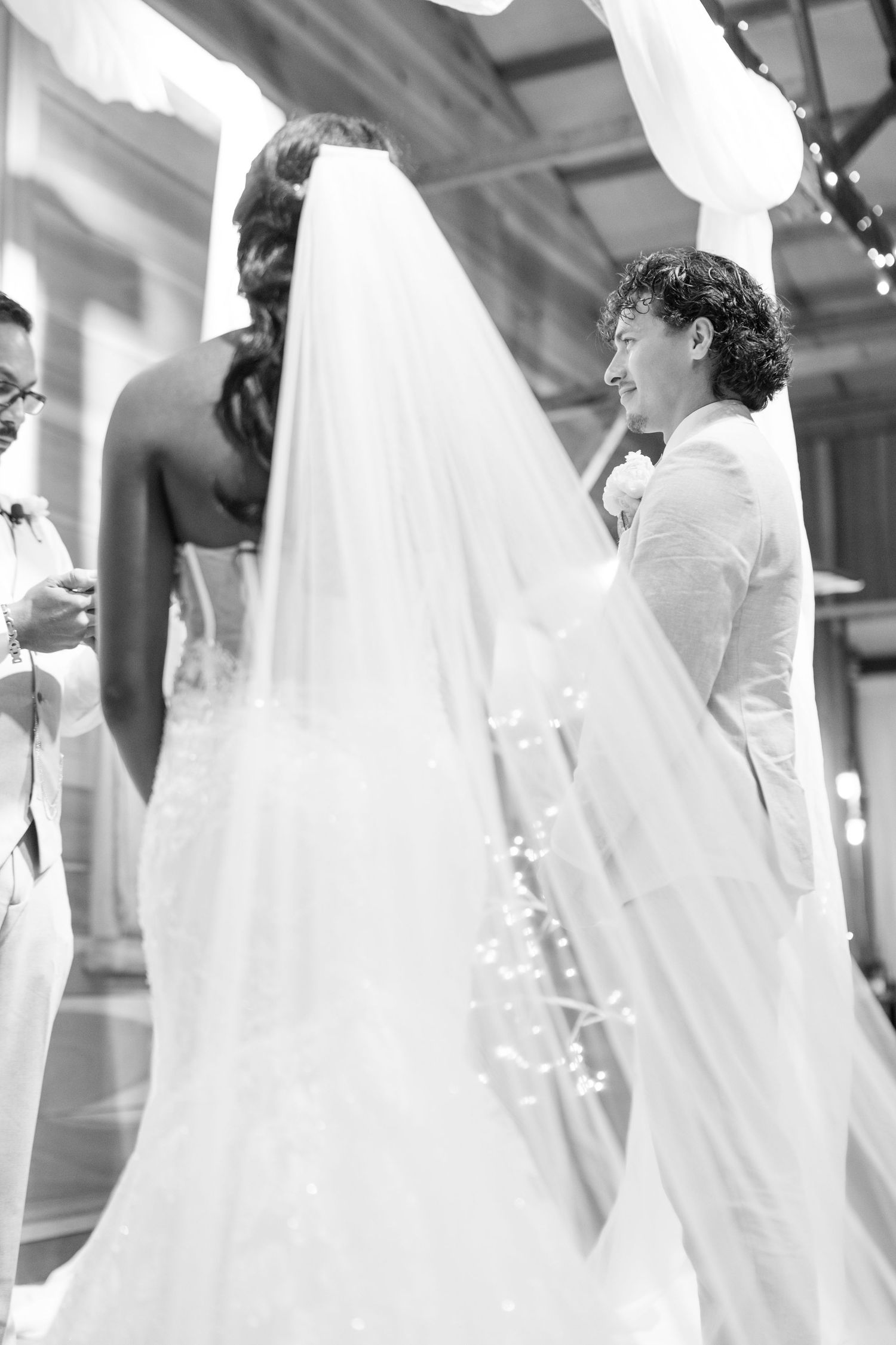 Black and white photo of two brides at wedding ceremony, one in strapless gown with long veil.