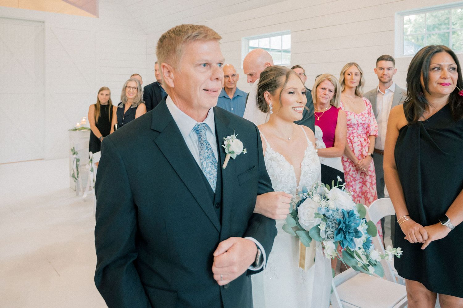 Wedding guests gather in a sunlit church venue decorated with floral arrangements and a wooden cross.