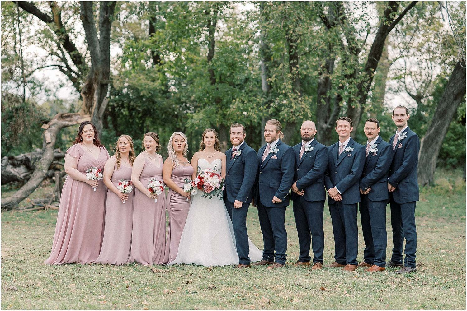 Wedding party lined up outdoors with bridesmaids in pink dresses and groomsmen in navy suits.