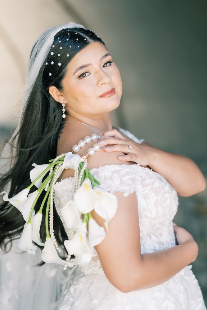 Artistic bridal photoshoot with white lilies and pearl accessories against soft blurred background.