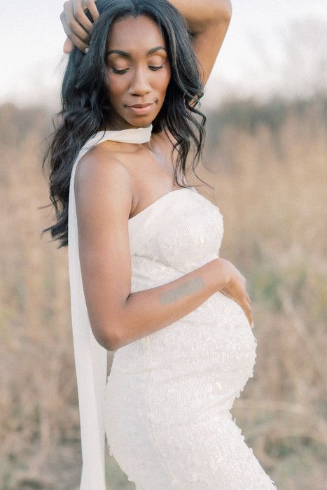 Expectant mother in flowing white dress poses gracefully in a natural outdoor setting during maternity photoshoot.