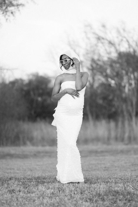 A figure in white fabric poses expressively against a natural outdoor backdrop.