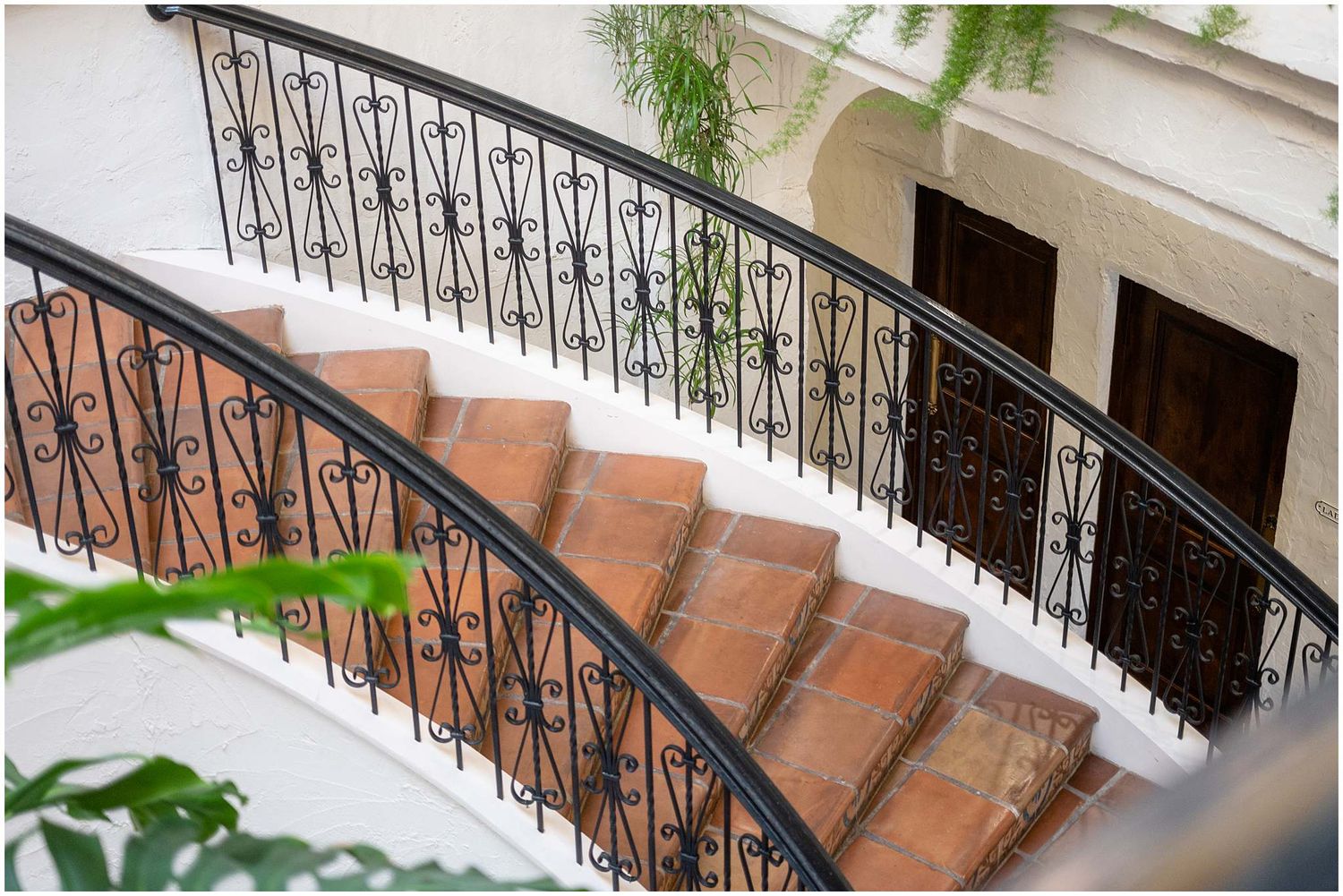Elegant black wrought iron stair railing with ornate scrollwork details against a light stone wall.